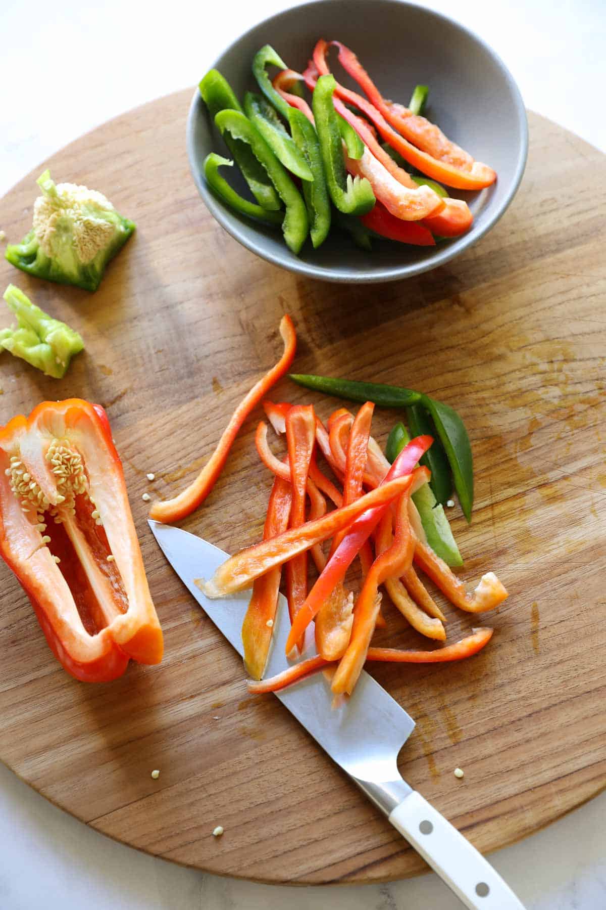 Slicing Bell Peppers into Strips on a Cutting Board with a Chef's Knife