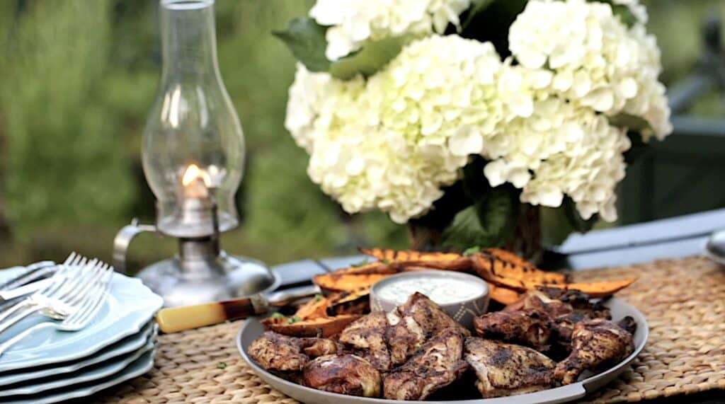 Grilled chicken and sweet potatoes on a table outside with flowers