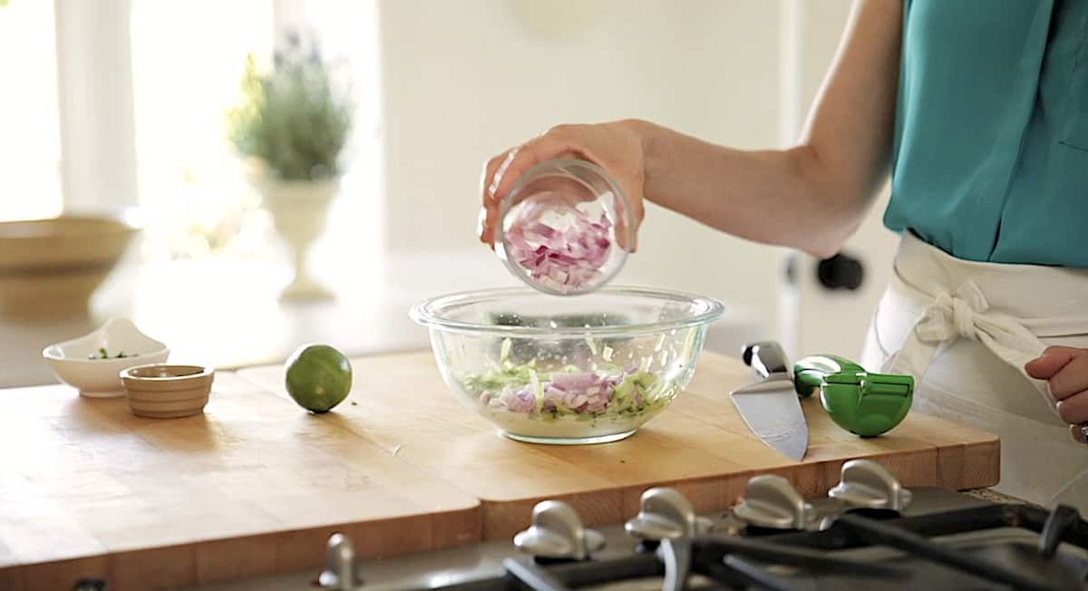 Adding red onion to a bowl with yogurt and cucumber in it