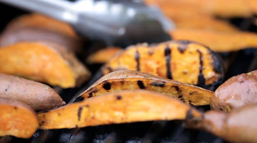 Turning sweet potatoes on a BBQ grill 