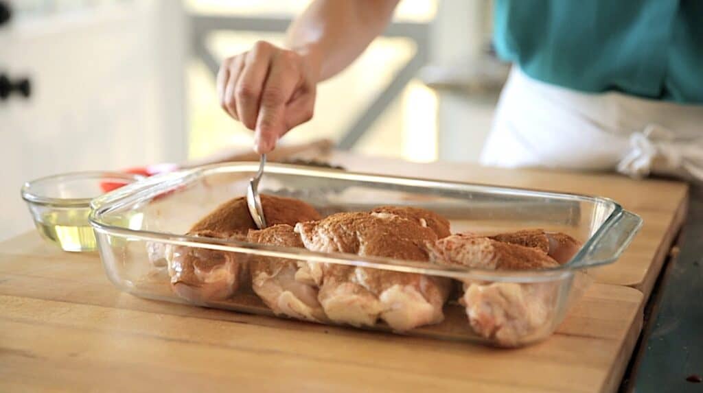 adding cinnamon rub to raw chicken in a casserole dish