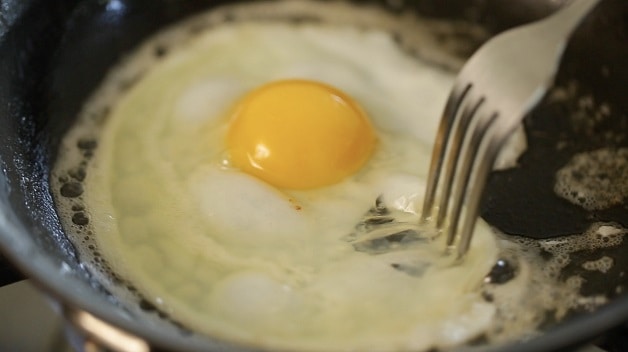 Fork shifting egg white inside of pan