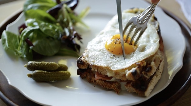 Slicing into Croque Madame sandwich with a fork and knife