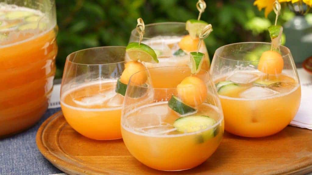 Glasses filled with canteloupe cucumber agua fresca garnished with melon balls and sliced cucumbers