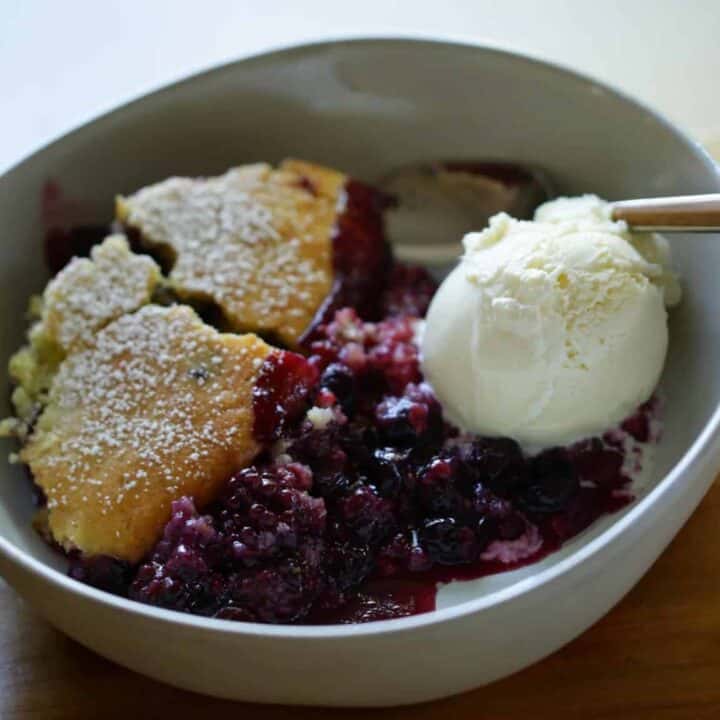 Triple Berry Campfire Cake Recipe in a white pottery bowl with a scoop of vanilla ice cream