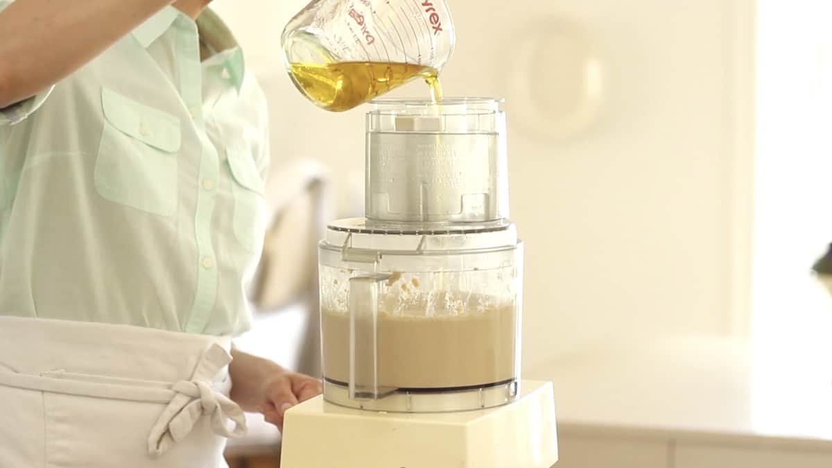 adding olive oil to a food processor with chickpeas