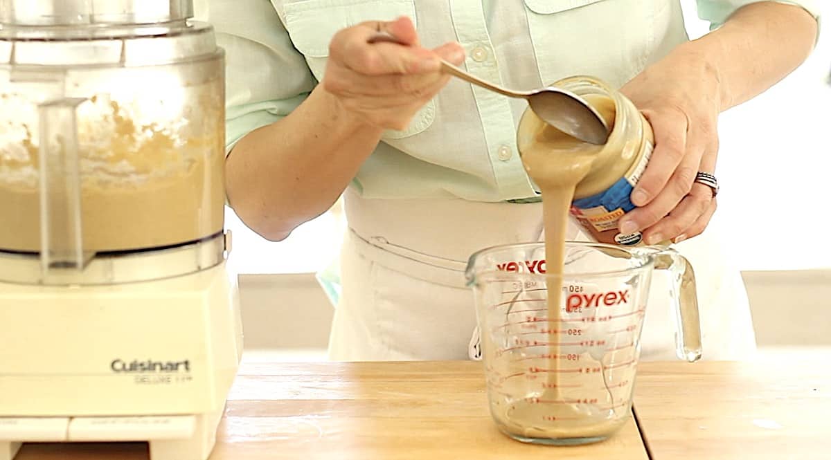 a person measuring out tahini in a Pyrex pitcher