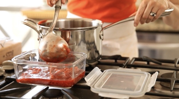 adding strawberry sauce to a glass container with a ladel