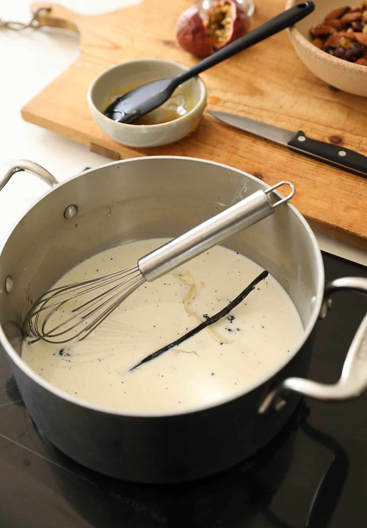 A milk mixture simmering with a vanilla bean pod simmering on cooktop.