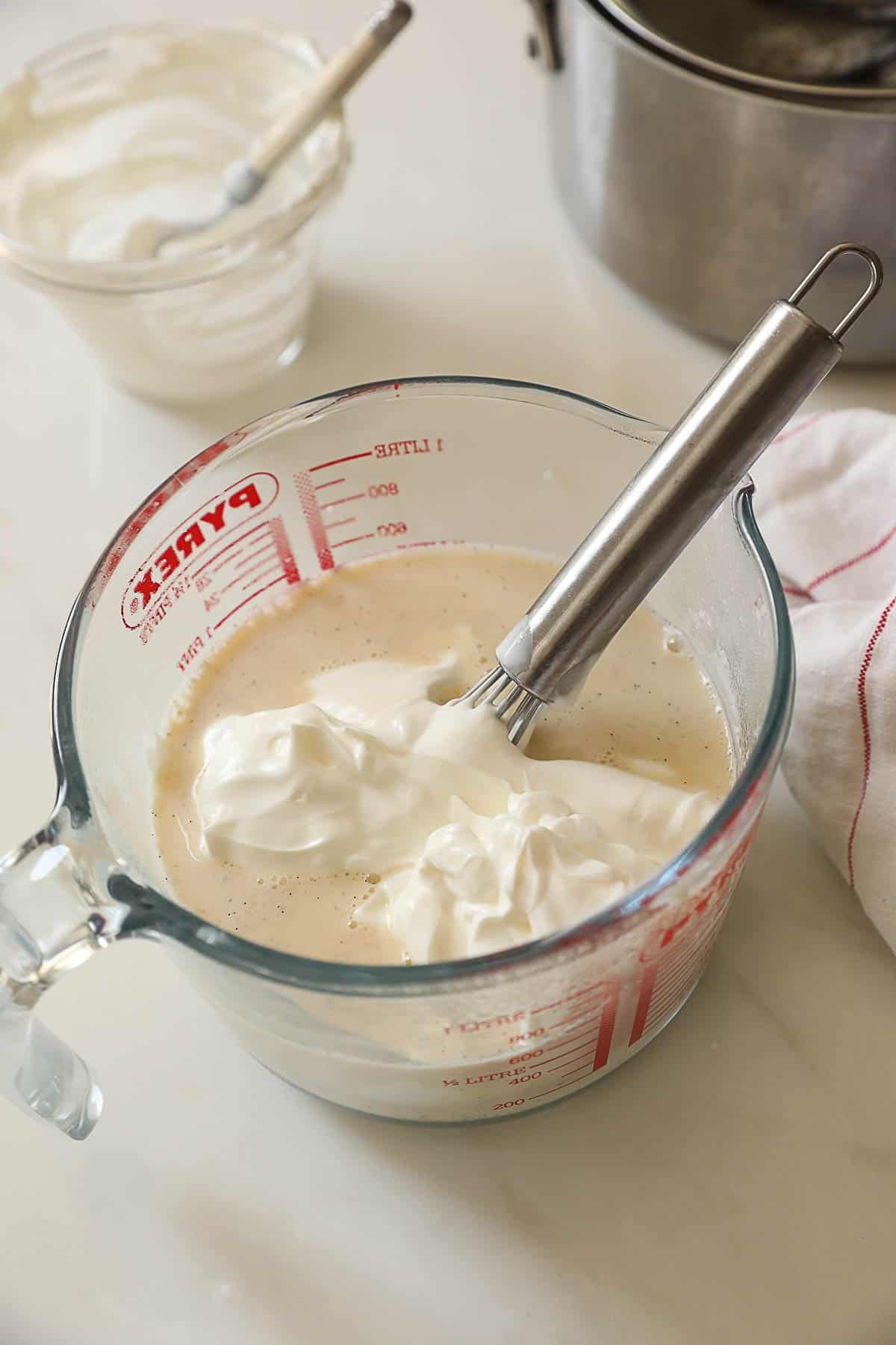 Greek yourt added to a sweetened milk and vanilla mixture in a large Pyrex pitcher.
