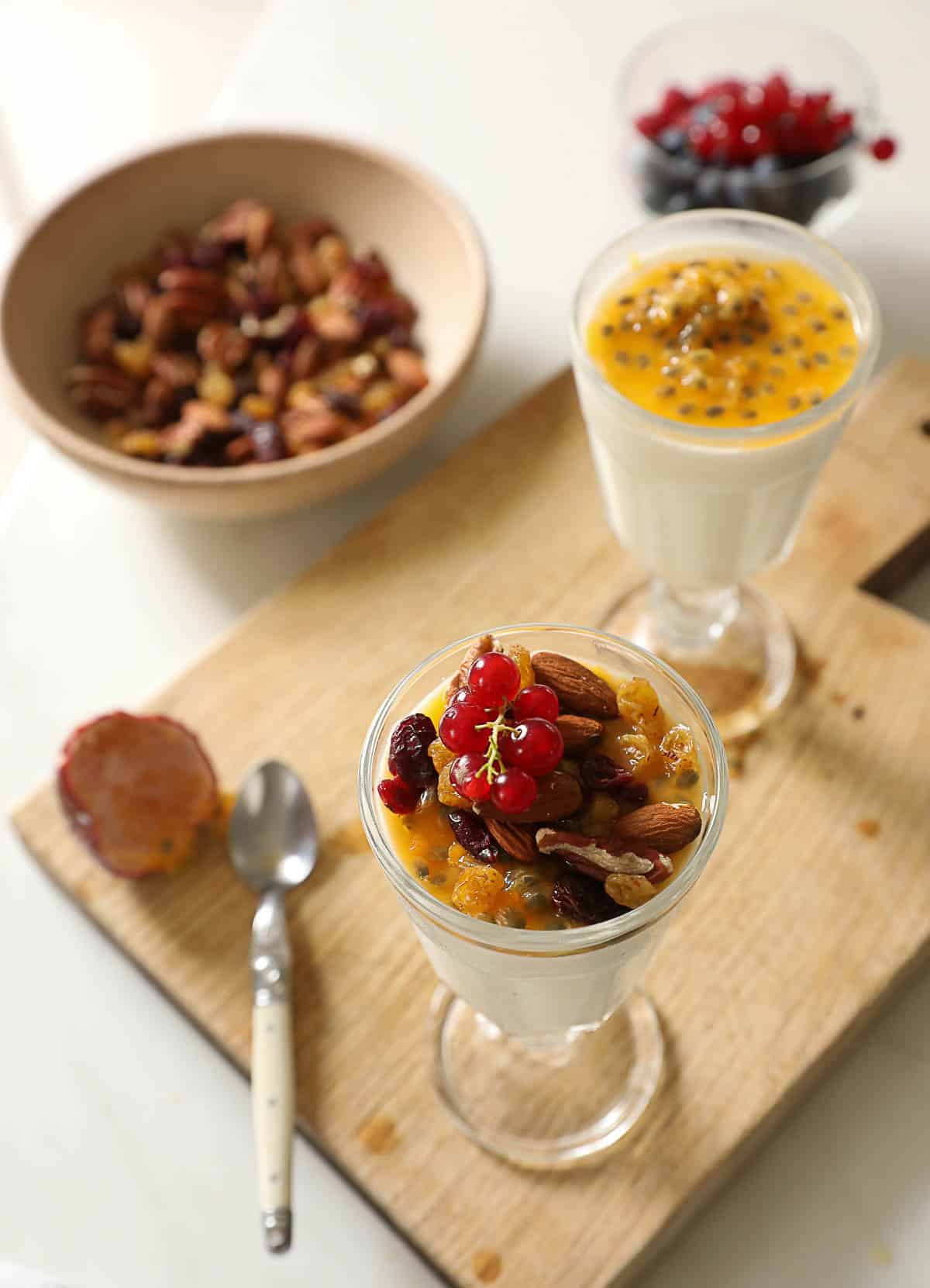 Yogurt panna cottas being topped with fresh fruit and nuts.