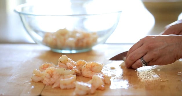 slicing cooked shrimp on a cutting board adding them to a bowl