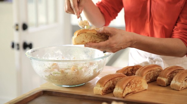 stffing a split top bun with a shrimp roll salad mixture