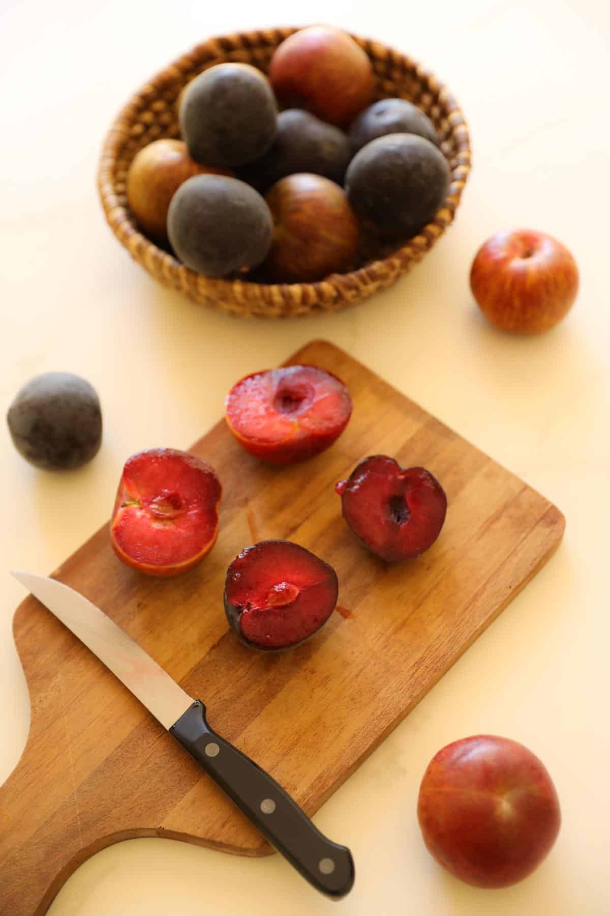 Red plums on a cutting board being sliced