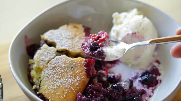 Ice cream melting on a berry cobbler with a spoon taking a bite