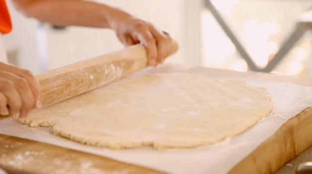 Rolling galette dough out on parchment paper with a rolling pin