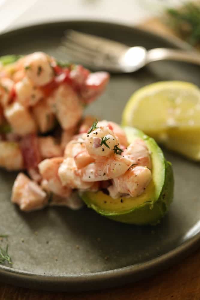A stuffed shrimp avocado on a plate with lemon slices.