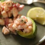 An avocado stuffed with shrimp salad on a plate with lemon.