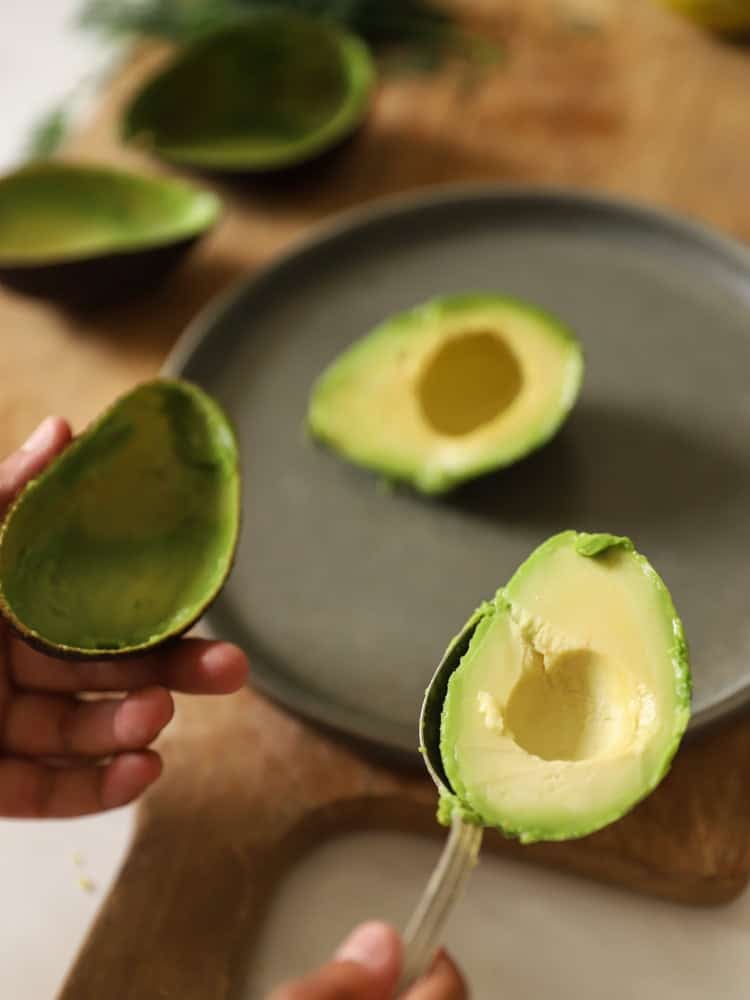 A person spooning out an avocado from it's shell with a large spoon.