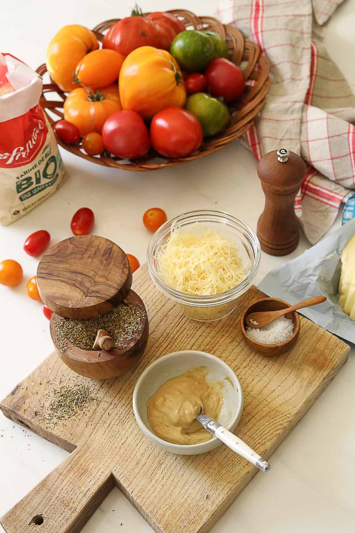 Flour, heirloom tomatoes, cheese and herbs laid out on a counter.