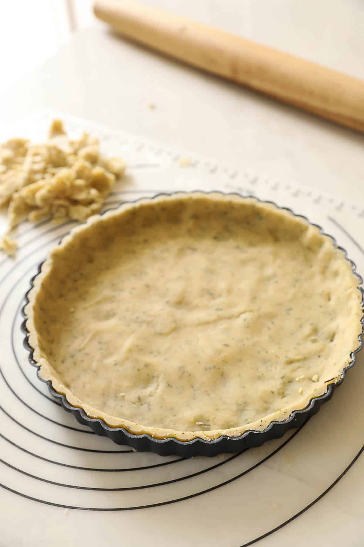 a tart tin fitted with pastry dough on a pastry mat.