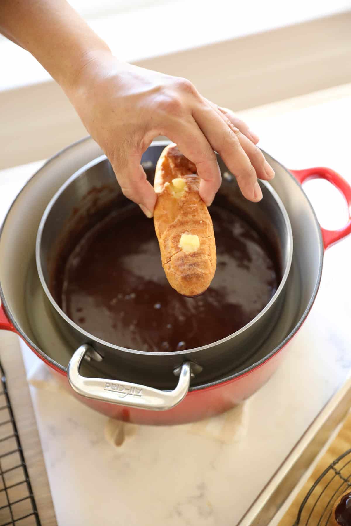 an eclair shell being dipped in chocolate glaze