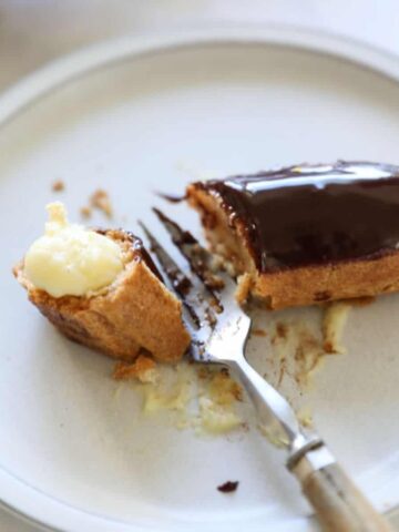 Chocolate eclair on a plate cut in half with a fork