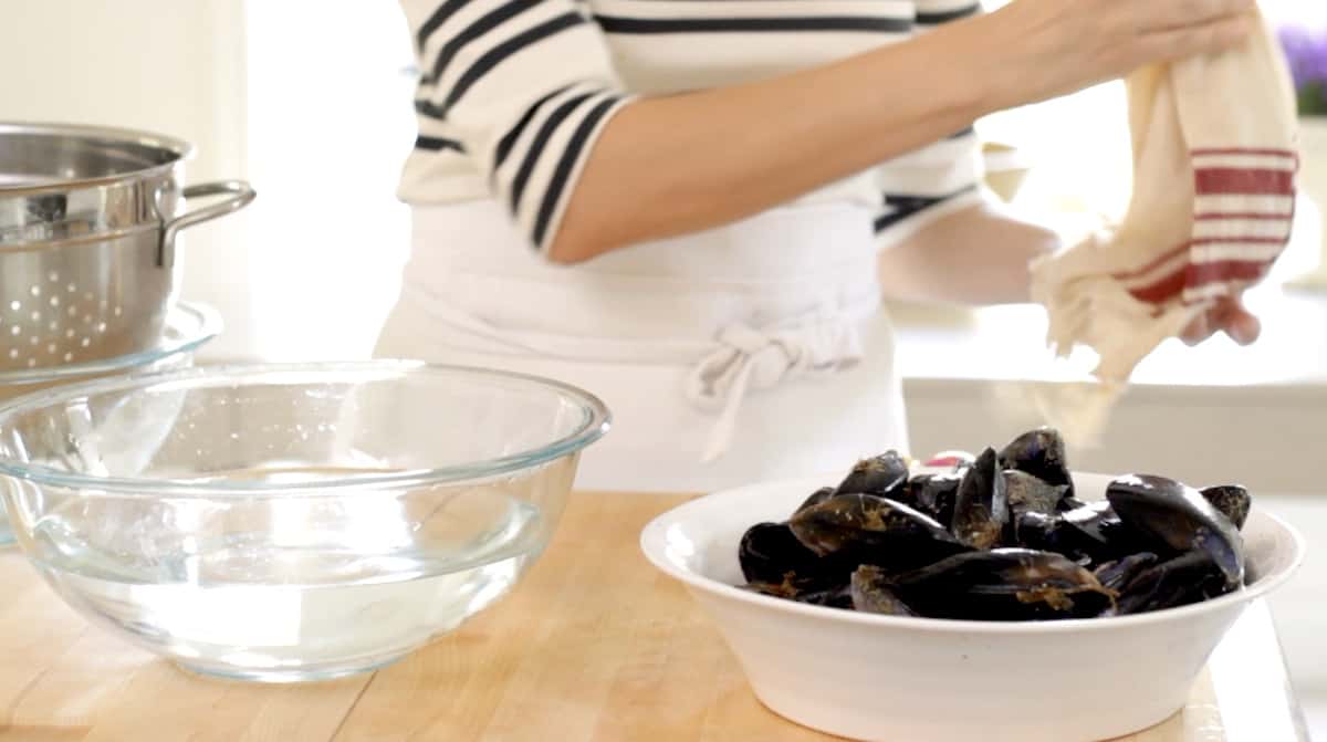 removing dish towel from a bowl of fresh mussels next to a bowl of fresh water