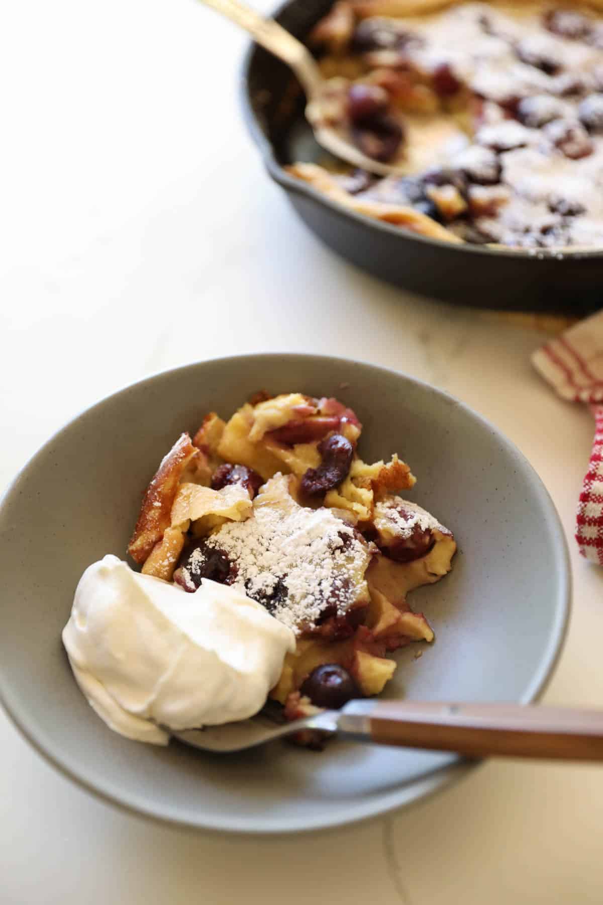 a serving of Cherry Clafoutis in a bowl with whipped cream