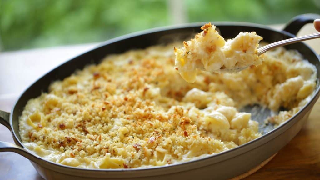 Large gratin pan full of baked mac and cheese with serving spoon showing a bite
