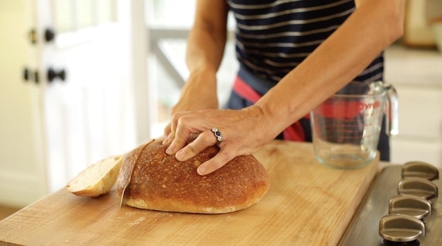 A person slicing a large loaf of bread with a bread knife