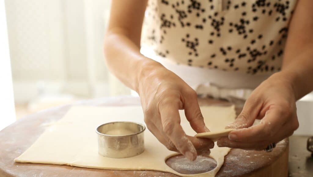 a person cutting out puff pastry rounds with a biscuit cutter