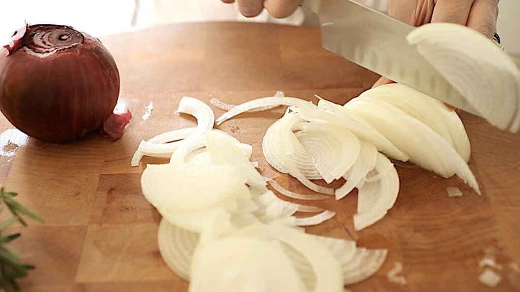 a person slicing white onions on a cutting board thinly