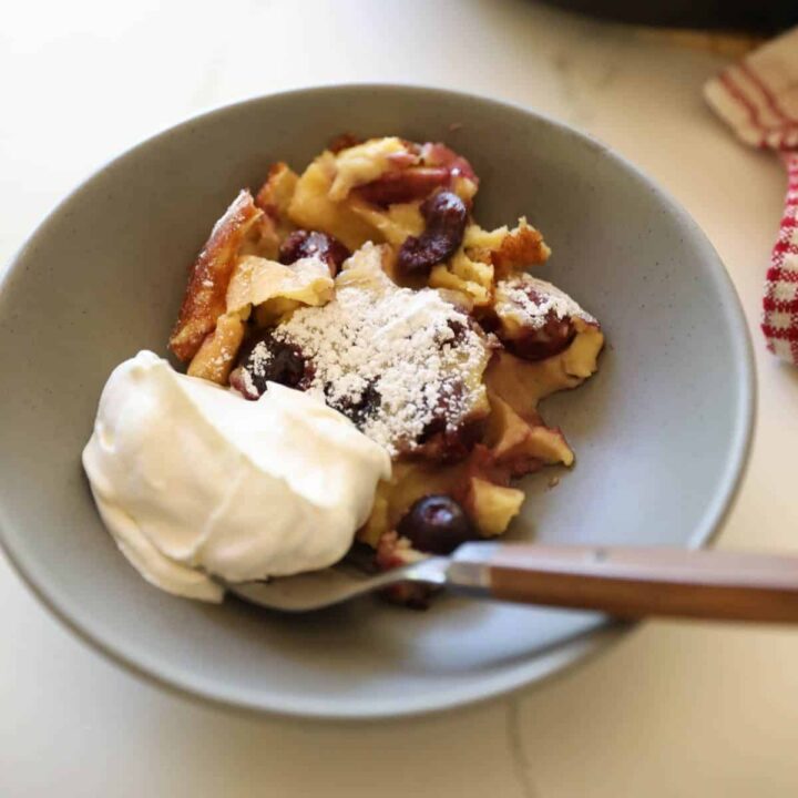 a serving of cherry clafoutis in a bowl with whipped cream