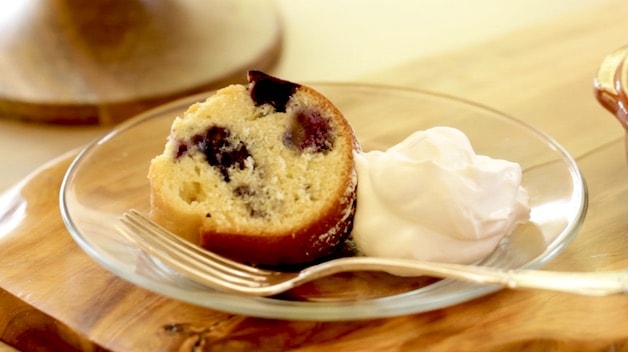 a slice of lemon blueberry bundt cake on a clear plate with whipped cream