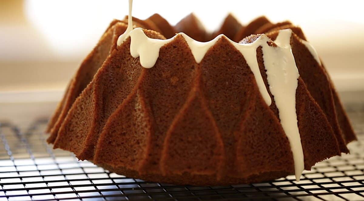 pouring cream cheese frosting on top of a bundt cake