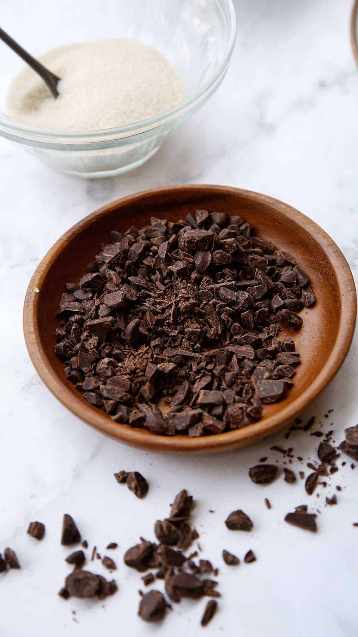 Dark Chocolate Chips chopped in place on a wooden plate with a bowl of sugar in the background