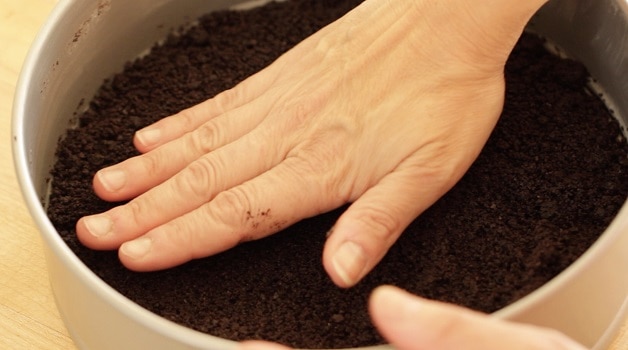 Pressing chocolate cookie crumbs into cheesecake pan for crust