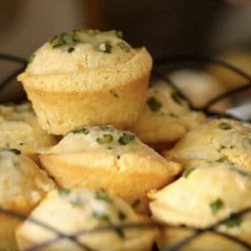 A close up of food, with BreaCornbread muffins topped with chives piled on a black wire cakestand