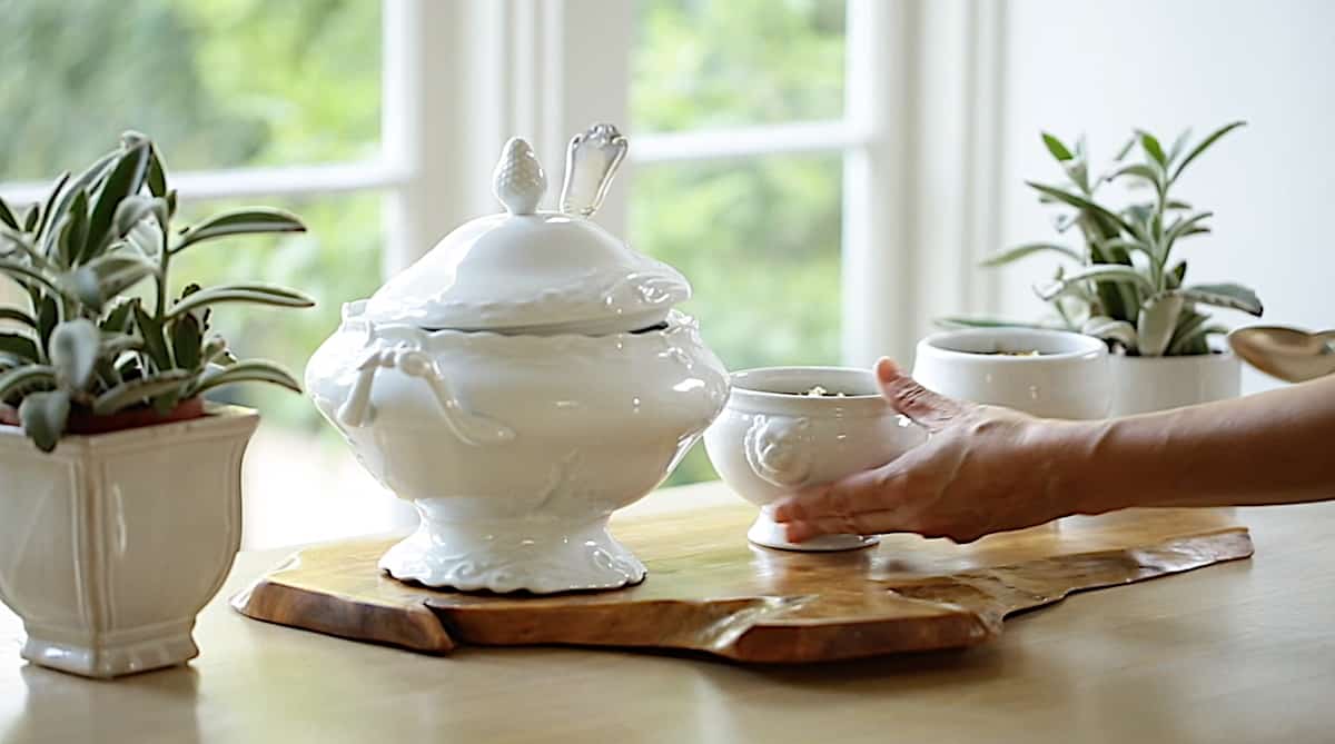 a person bring bowls of soup to a table set with a white French-style soup tureen