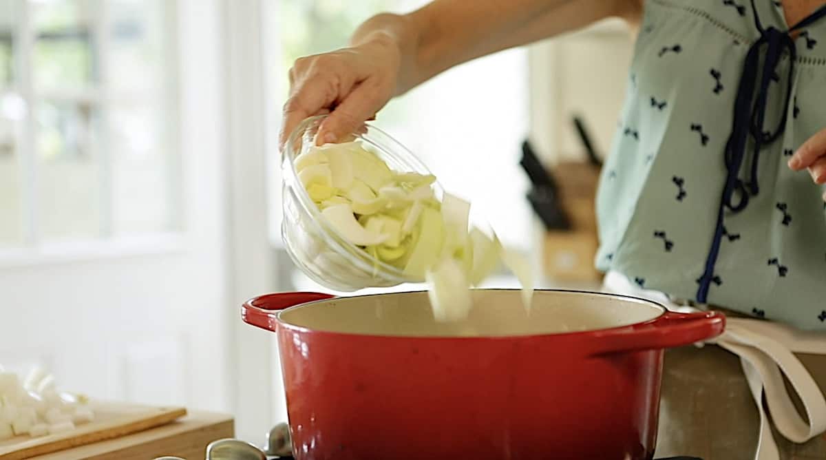 a person adding chopped leeks to a red Dutch oven