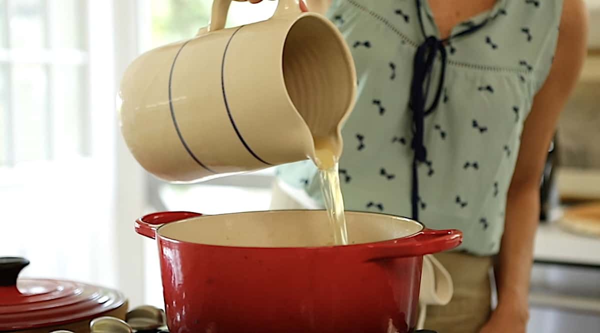 a person adding broth from a pitcher to a pot