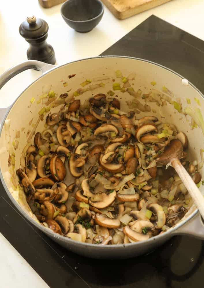 Mushrooms cooking in a pot with leeks, onions and garlic.