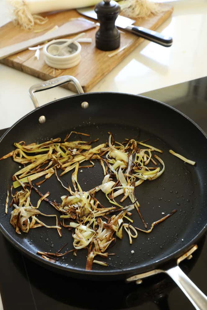 Thin leeks frying in a pan.