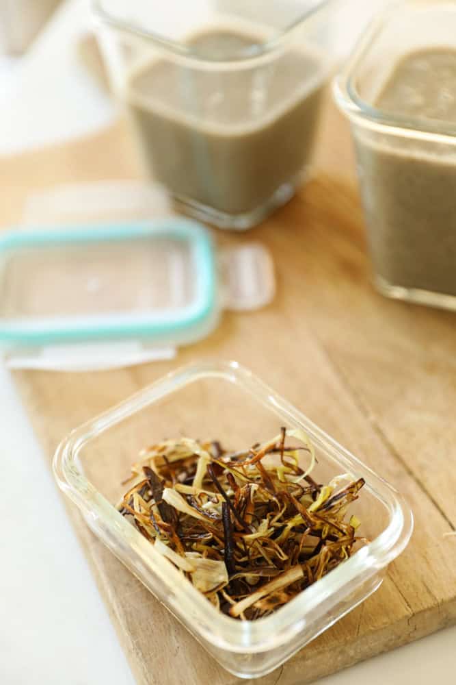 Mushroom soup being stored in glass containers with sautéed crispy leek garnishes.