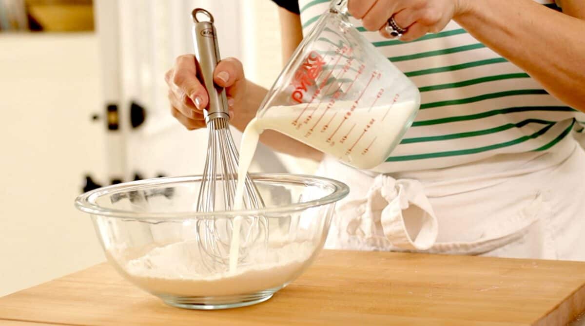 Mixing milk into flour in a large clear bowl