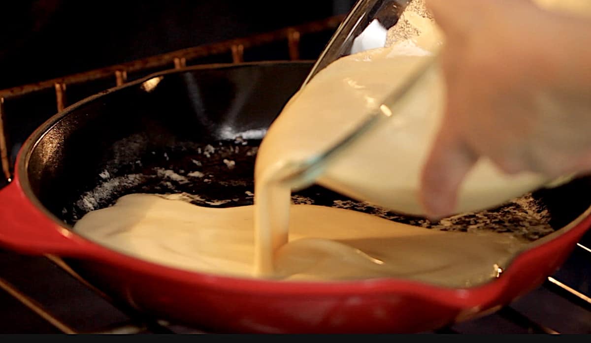 pouring batter into a cast iron skillet in the oven