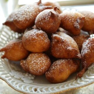 Apple Fritters on a white cake stand dusted with powdered sugar