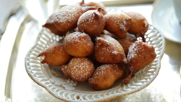 Apple Fritters on a white cake stand dusted with powdered sugar