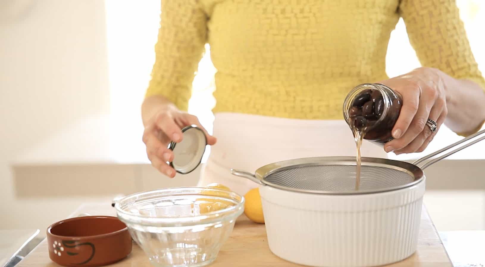 A person draining olives from a jar into a strainer